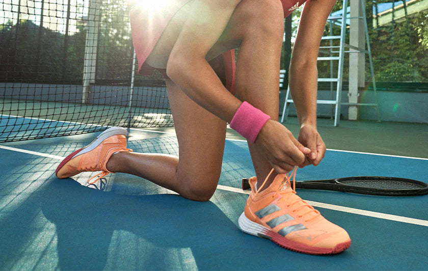 woman ties orange shoes in tennis court