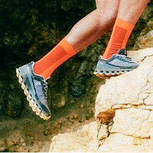 A person running up a rocky hill in On trail running shoes.