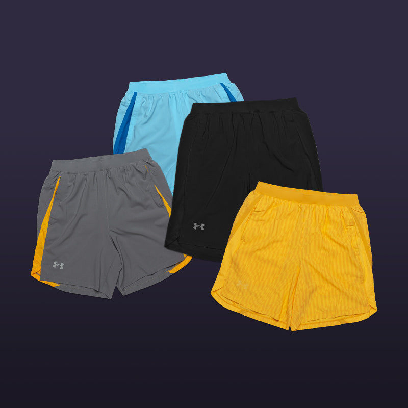 Four assorted pairs of men's Under Armour Launch Run Shorts in black, blue, gray and gold on a dark purple bacgkround.