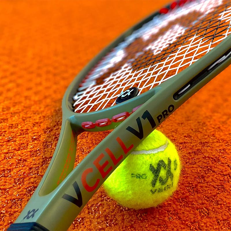 Volkl V-Cell V1 Pro Green tennis racquet and Volkl tennis ball on a red clay tennis court.